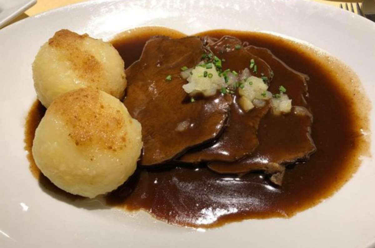 Plate of traditional German-style roast beef in a rich dark gravy, served with potato dumplings called Sauerbraten