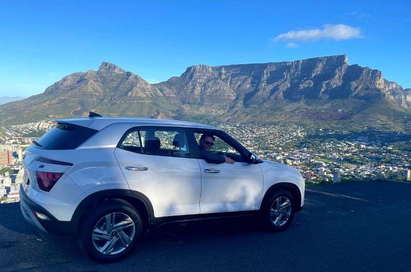 Photo of a man in a car with Table Mountain in the background, Cape Town