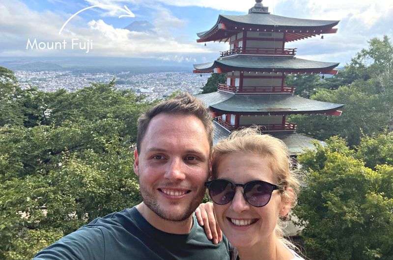 Tourists in front of Kitaguchi Hongu Fuji Sengen Shrine in Japan with Mt. Fuji in the background barely visible through the clouds