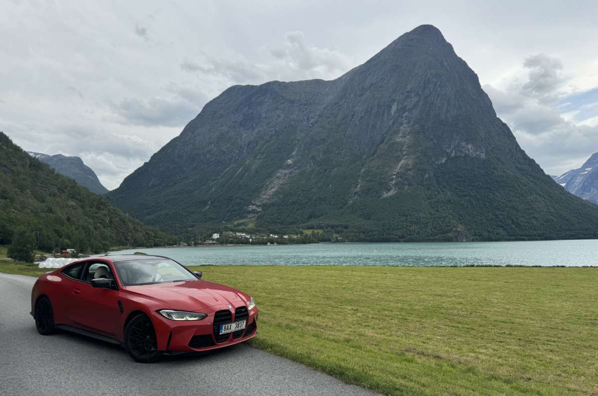 a photo of a red car in the middle of the road with a lake and a mountain in the background, Norway, photo by Next Level of Travel