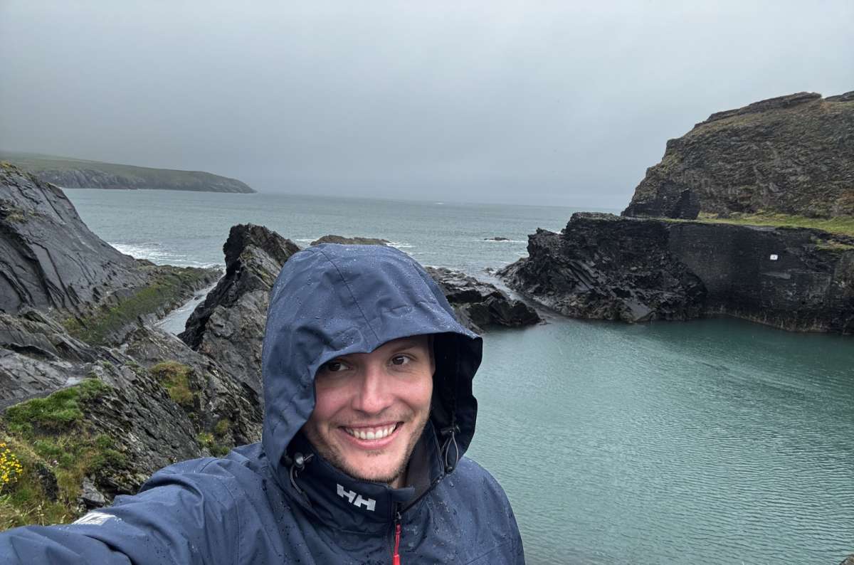 Traveler in a rain jacket overlooking a rocky cove on the Welsh coast during cloudy weather, a photo by Next Level of Travel