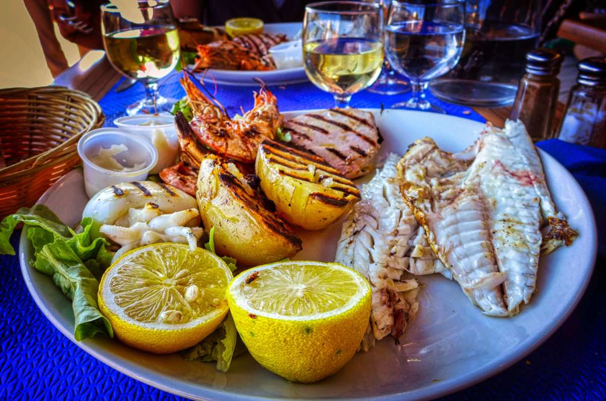 Seafood platter with grilled shrimp, fish, vegetables, and lemon halves, served with white wine