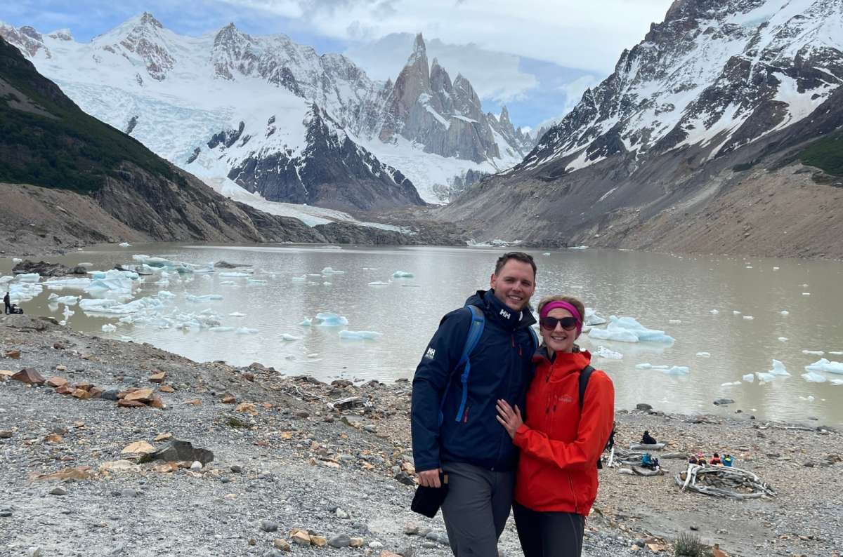 Couple posing by a glacial lake and snow-covered mountains in the background, Patagonia, photo by Next Level of Travel