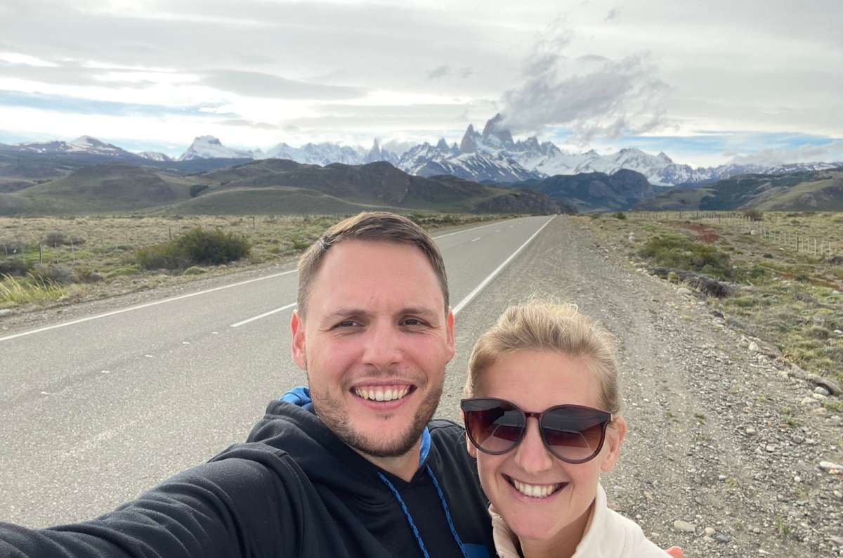 Smiling couple taking a selfie on a road with Mount Fitz Roy in the background in Patagonia, photo by Next Level of Travel