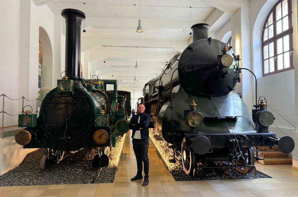 a man posing between two trains at the Deutsche Bahn Railway Museum, Germany