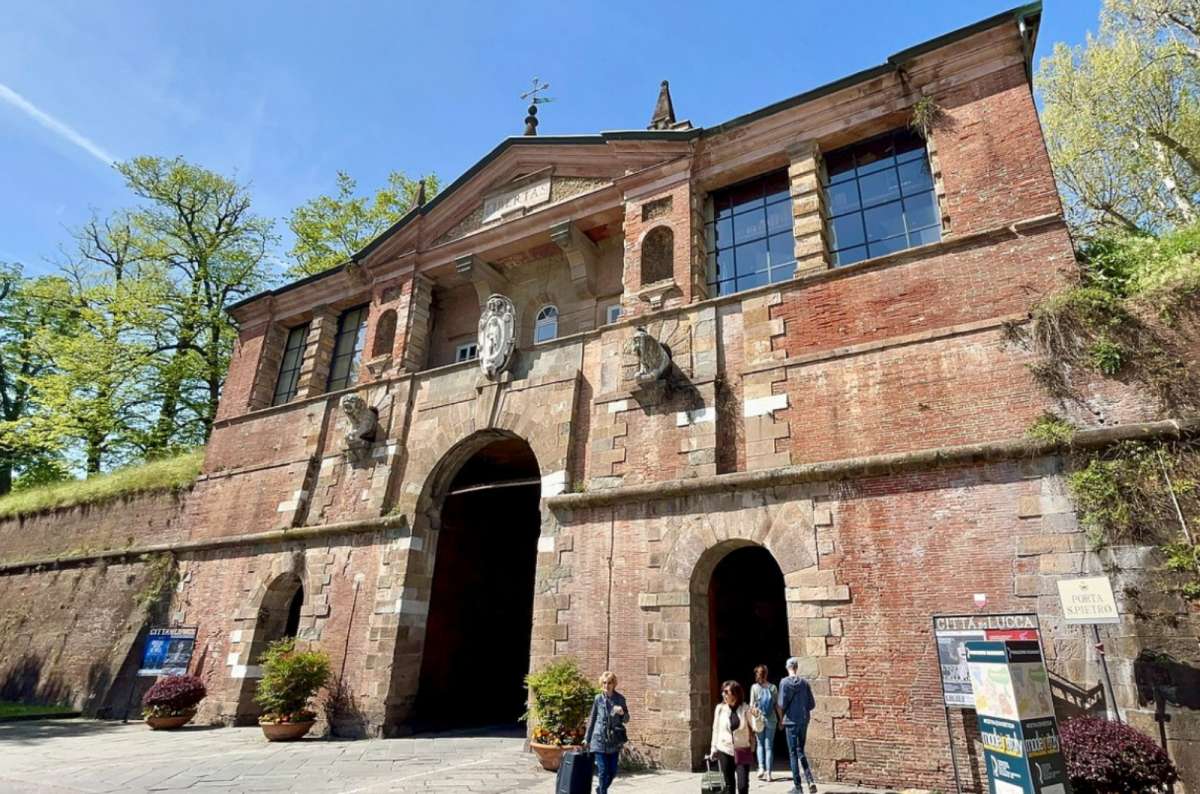 Brick gateway of Porta San Pietro in Lucca, with pedestrians walking through and signs pointing to the historic center and city walls