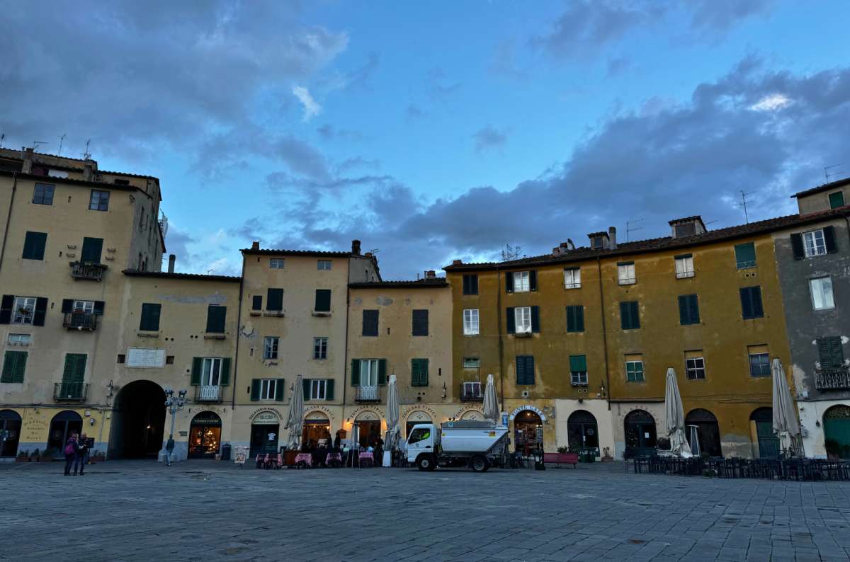 Evening view of Lucca’s Piazza dell’Anfiteatro with quiet cafés and moody skies, photo by Next Level of Travel