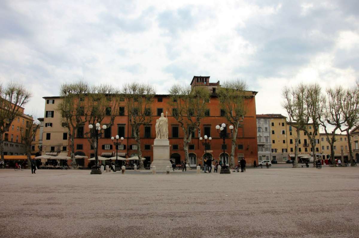 Lucca’s largest square, Piazza Napoleone, with a central statue, leafless trees, and people walking near surrounding buildings, Italy