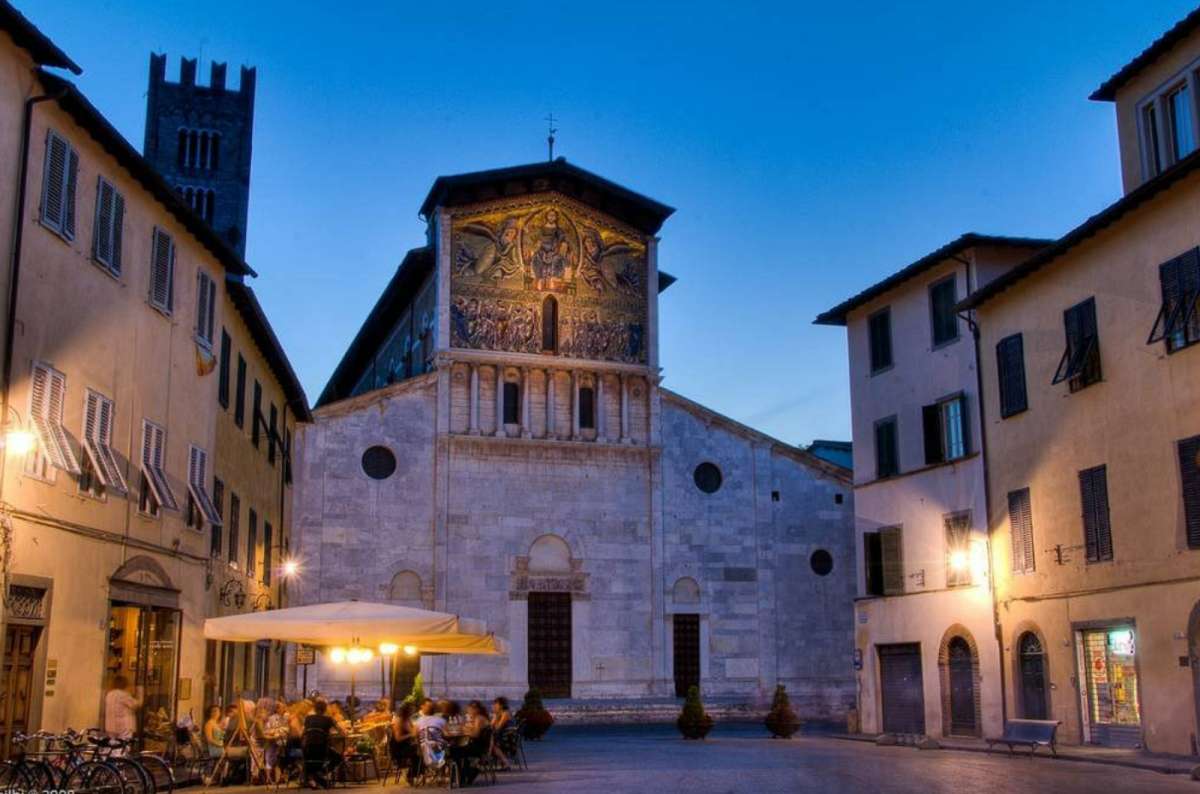 vening view of Basilica di San Frediano in Lucca, with its illuminated golden mosaic façade and a nearby outdoor café filled with diners