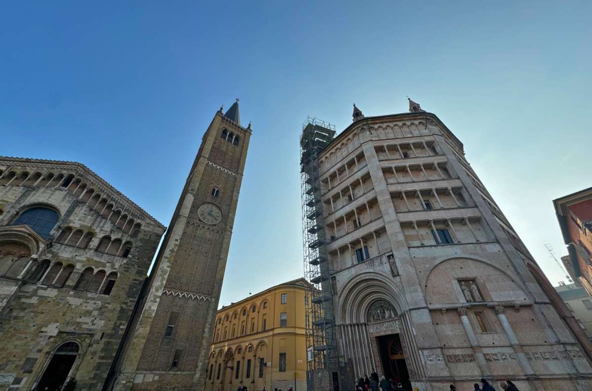 View of Parma Cathedral, the adjacent bell tower, and the pink octagonal Baptistery of Parma under a clear blue sky, Italy travel blog, photo by Next Level of Travel
