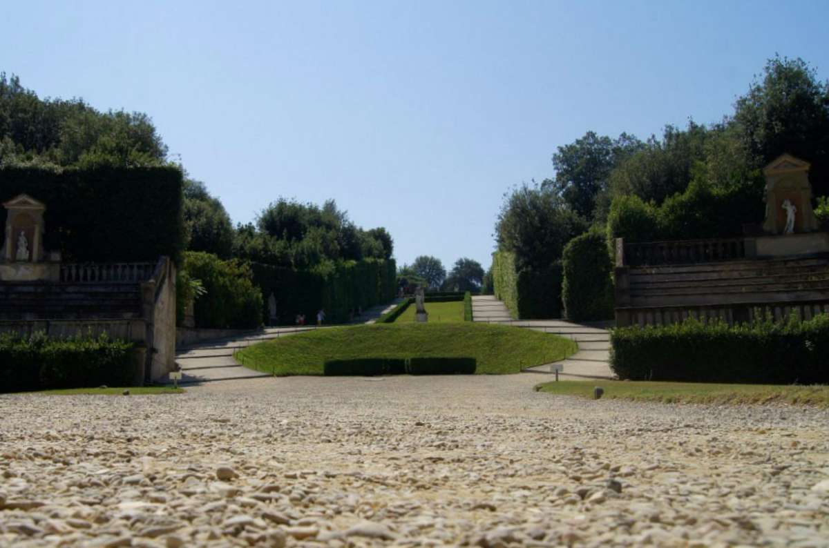 View from the ground of a symmetrical gravel path leading through hedges and classical statues in Boboli Gardens, Florence, Italy