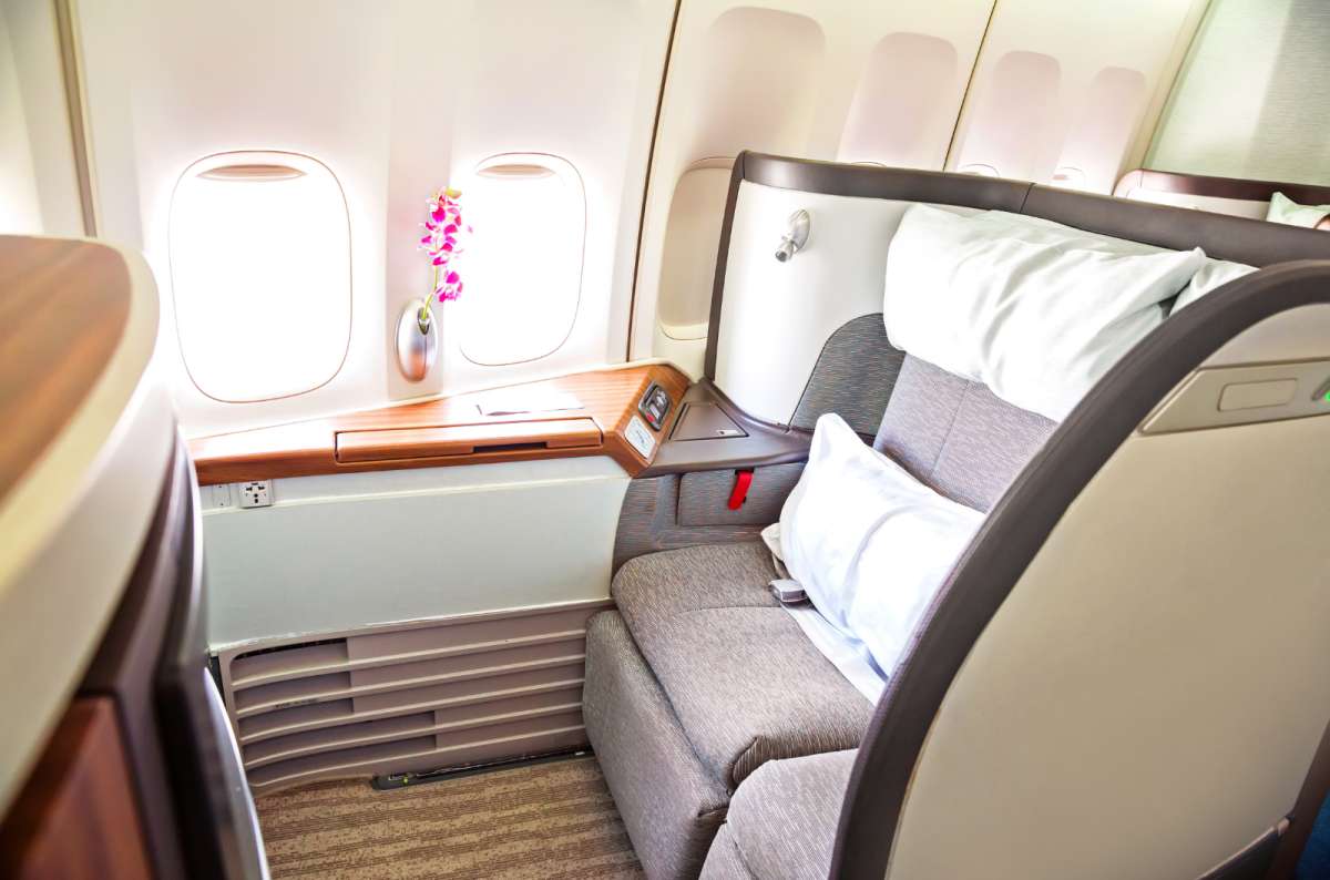 Luxurious first class airline suite with wide seat, plush pillows, wood accents, and flower by the window