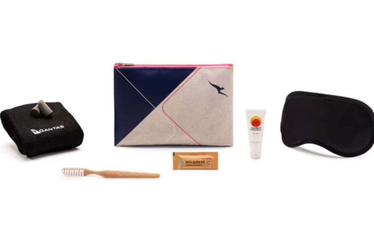 Qantas Premium Economy amenity kit with earplugs, eye mask, socks, toothbrush, toothpaste, lip balm, and a stylish travel pouch