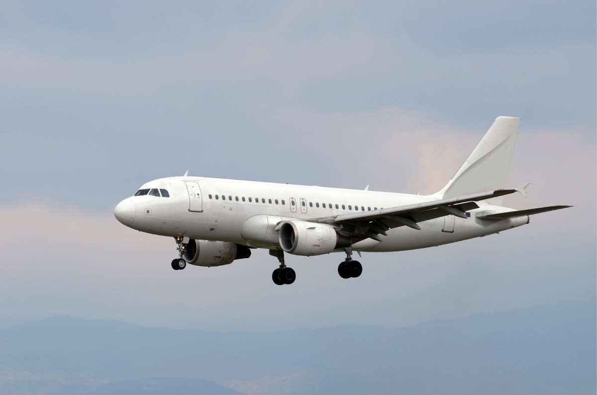 White passenger airplane landing with landing gear extended, mountains in the background, cloudy sky