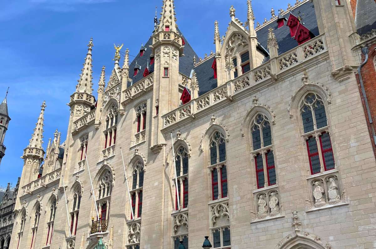 Gothic-style facade of the Bruges Provincial Palace with ornate windows, spires, and red-framed windows, photo by Next Level of Travel