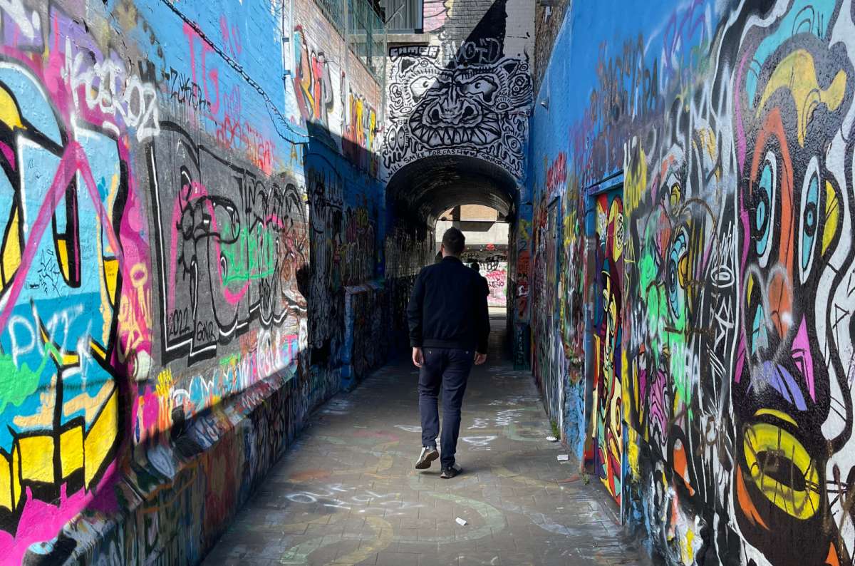 a photo of a tourist from the back walking through Werregarenstraat–a street covered in graffiti, Ghent, Belgium, photo by Next Level of Travel