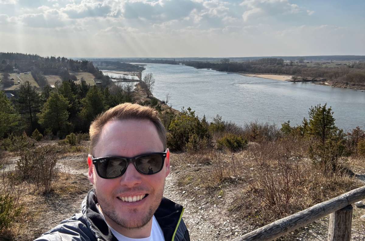 a photo of a tourist posing in front of beautiful Polish scenery with a river visible in the background, Lublin, Poland, photo by Next Level of Travel