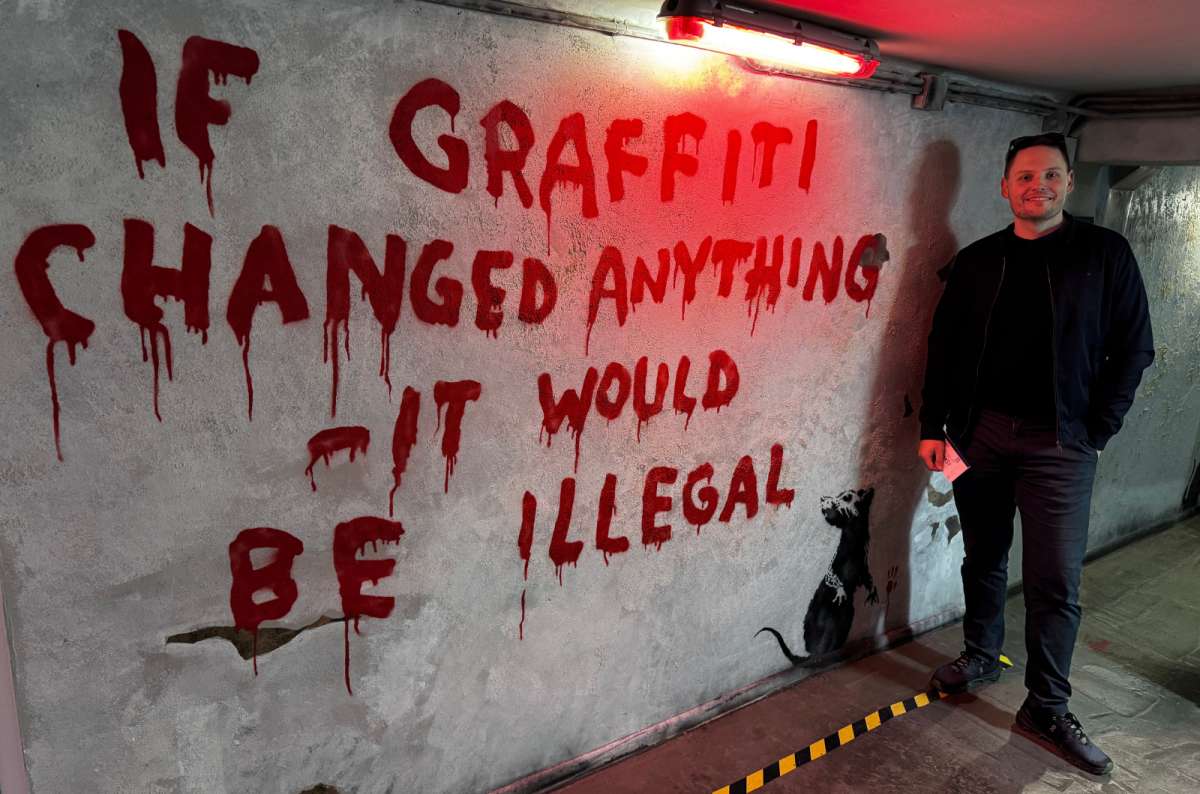 a photo of a tourist posing in front of a graffiti wall at the Banksy Museum in Krakow, Poland, photo by Next Level of Travel
