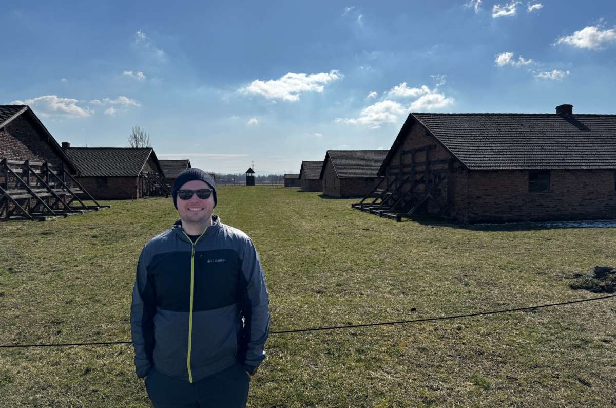 a photo of a tourist posing in front of the barracks on the Auschwitz camp, Oświęcim, Poland, photo by Next Level of Travel