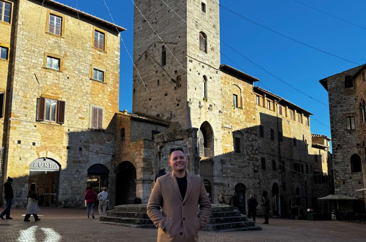 a photo of a tourist posing at Piazza della Cisterna on a sunny fall afternoon, San Gimignano, Italy, photo by Next Level of Travel