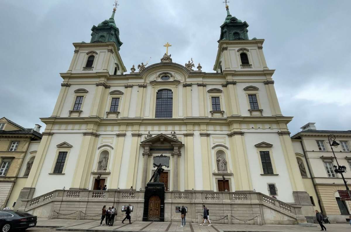 Holy Cross Church in Warsaw, Poland, a 17th-century Baroque building with twin green spires and statues above the main entrance