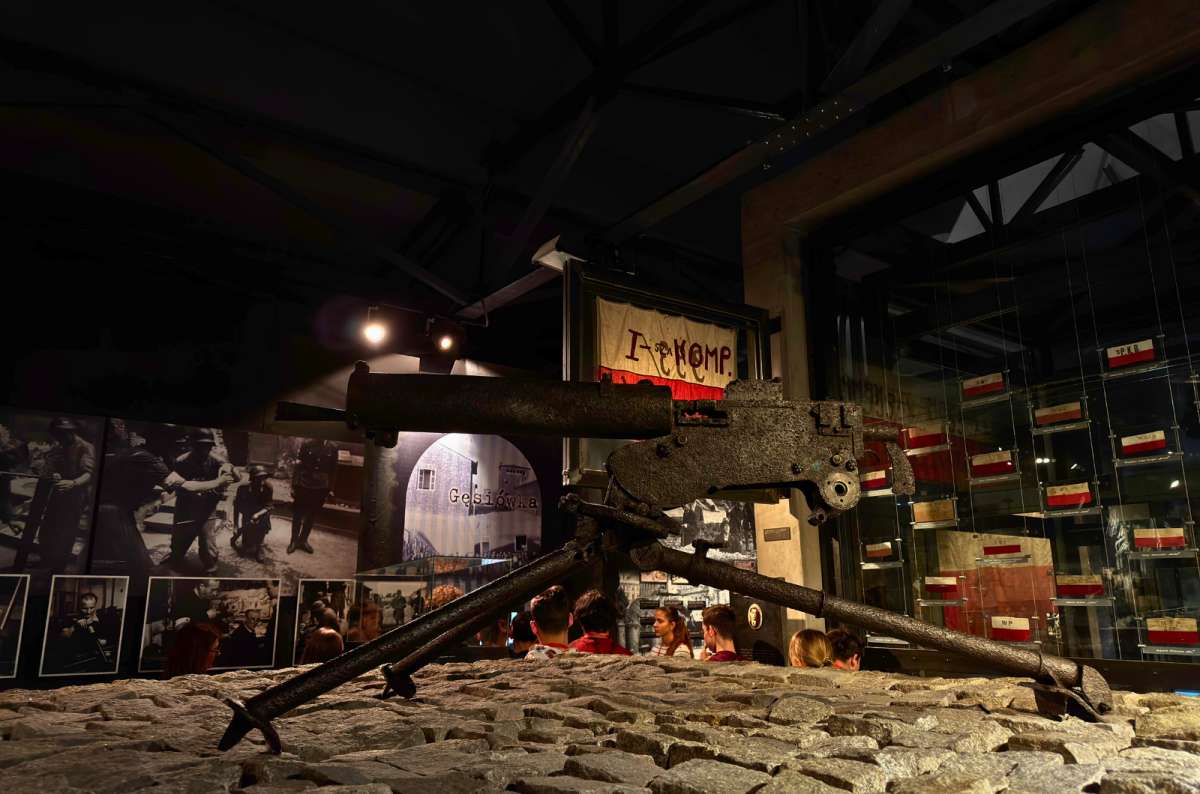 Rusted World War II machine gun displayed on cobblestones inside the Warsaw Uprising Museum, photo by Next Level of Travel