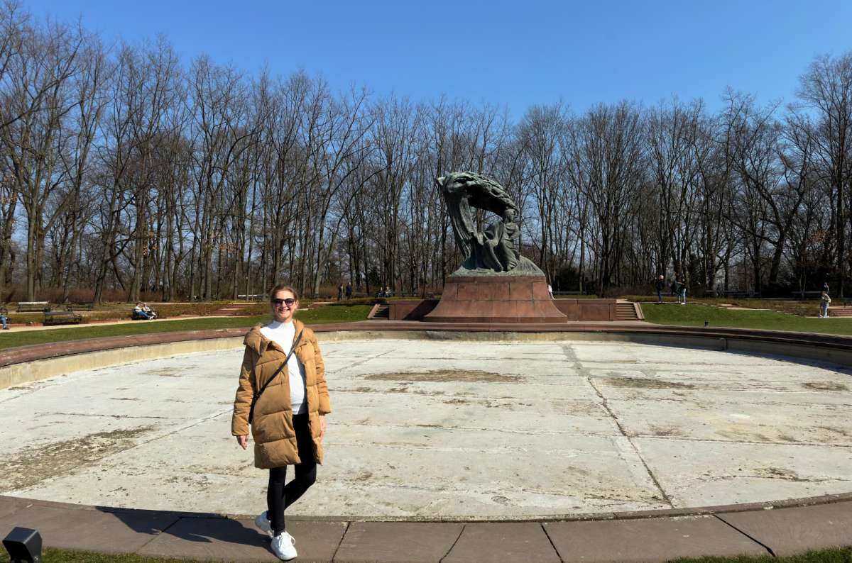 Visitor standing by the Fryderyk Chopin Monument in Łazienki Park, Warsaw, Poland, on a sunny day, photo by Next Level of Travel