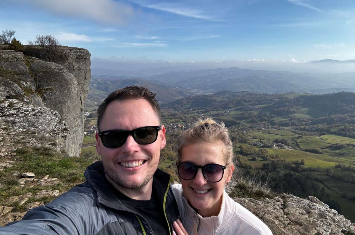 Two travelers smiling with the scenic view of Rocca di Bismantova cliffs and green hills near Modena, Italy, photo by Next Level of Travel