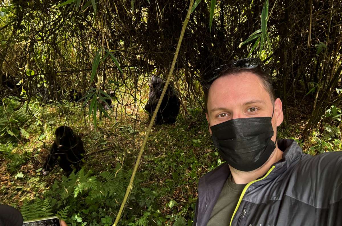  a photo of a tourist wearing a face mask posing with gorillas in the forest closeby in the background, Rwanda, photo by Next Level of Travel