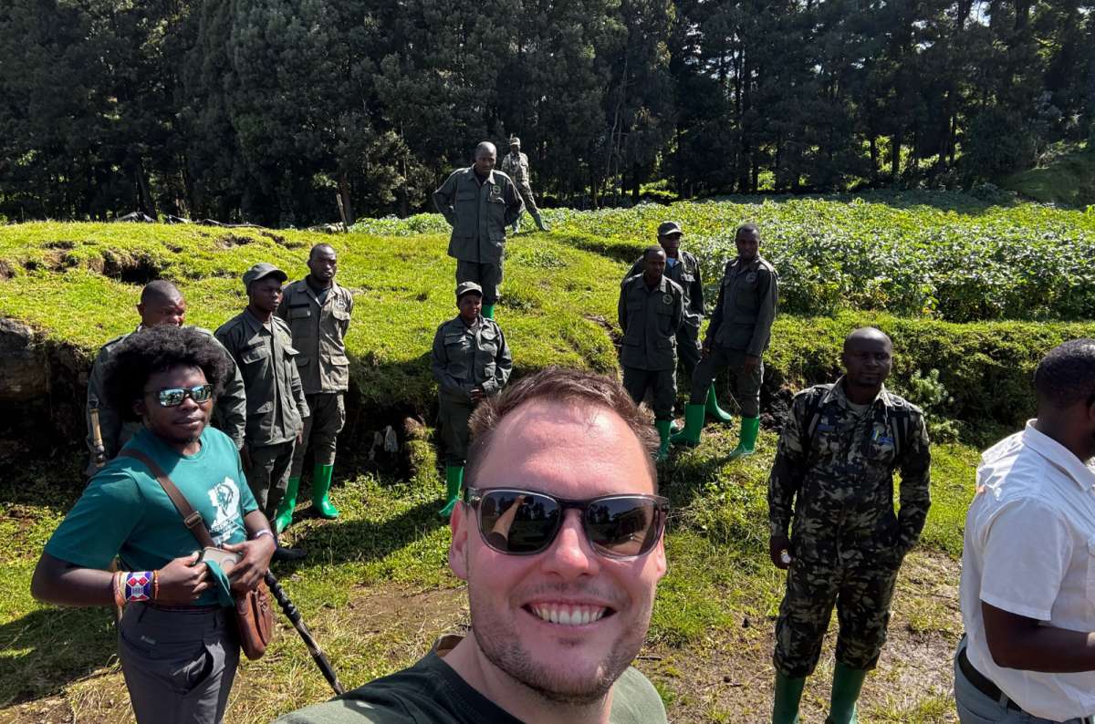 a photo of a tourist and a group of Volcanoes National Park rangers outside the forest after gorilla trekking in Rwanda, photo by Next Level of Travel