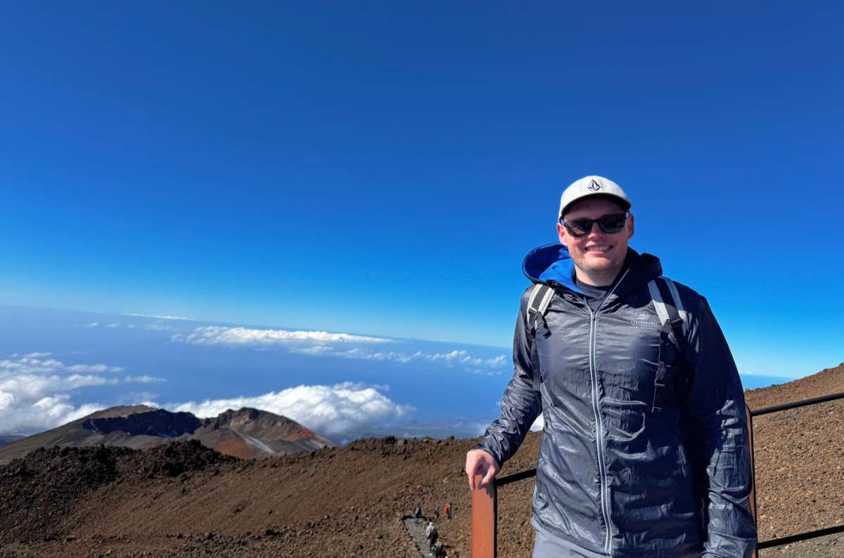 Hiker standing on volcanic terrain with clouds below at Mount Teide National Park, Tenerife, Spain, one of the most unusual tourist places in Europe, photo by Next Level of Travel