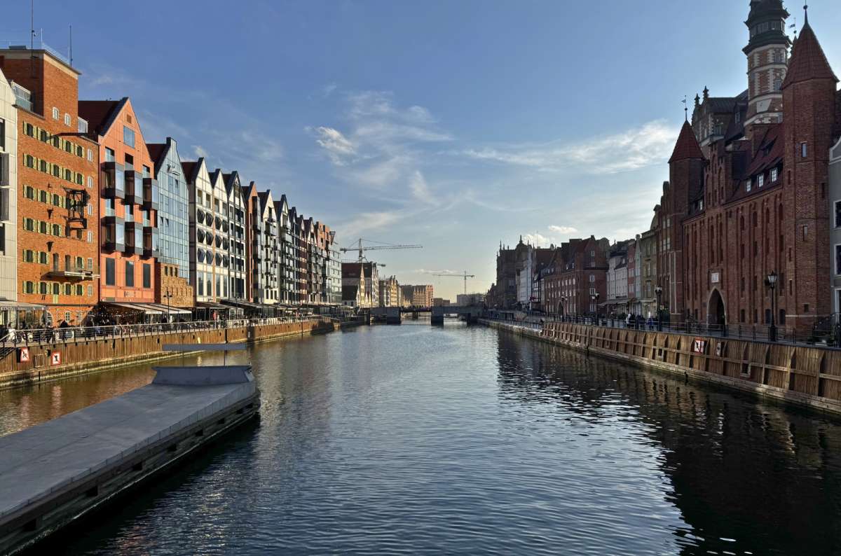A bridge over the Motława River in Gdansk Old Town, Poland, with historic red-brick buildings and modern waterfront architecture, photo by Next Level of Travel