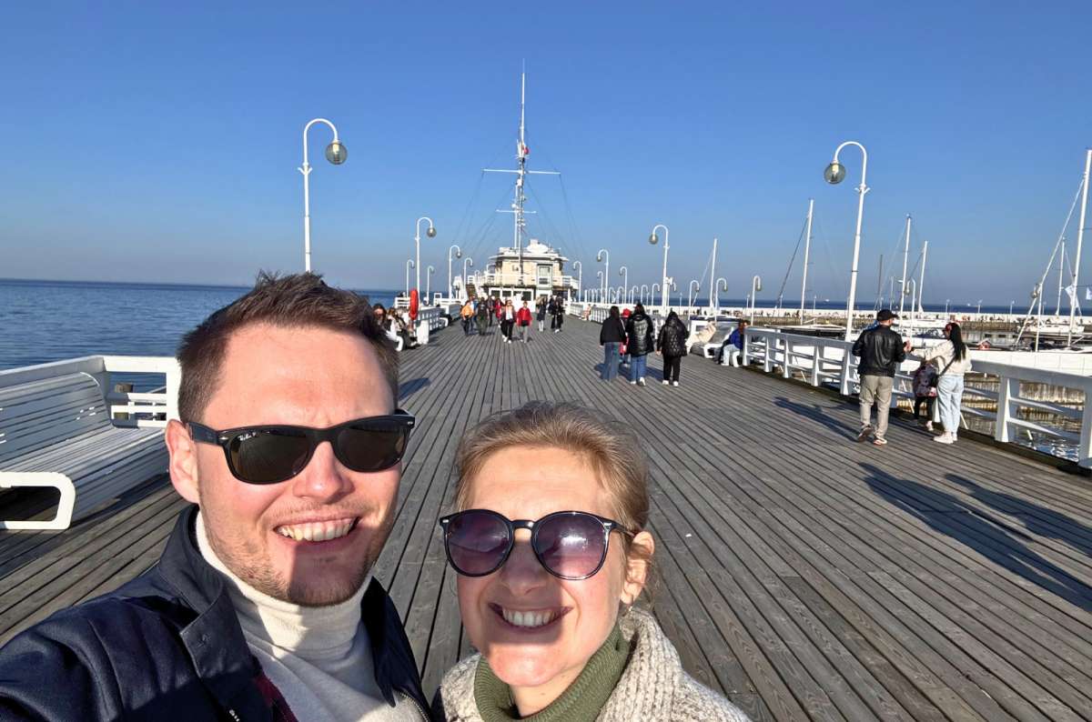 Couple standing on Sopot Pier (Molo w Sopocie) in Sopot, Poland, with the Baltic Sea and marina in the background, photo by Next Level of Travel