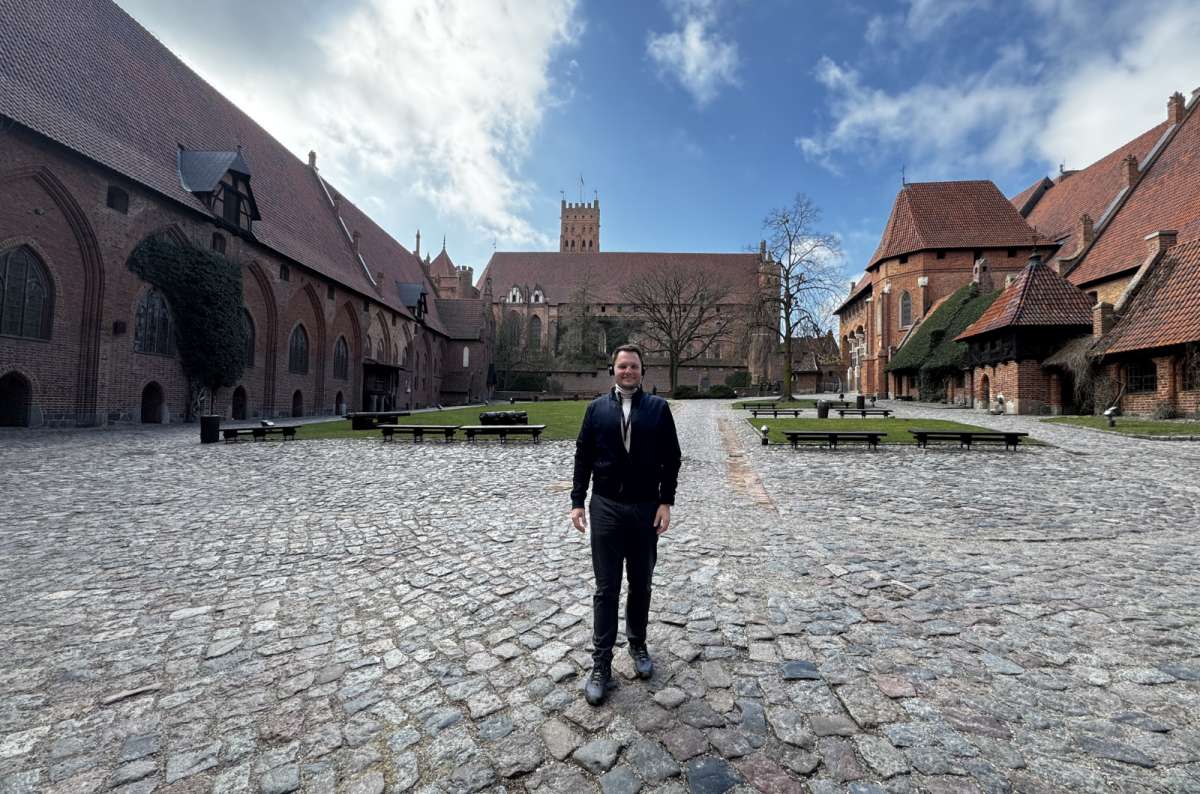 A photo of a tourist standing in front of the Malbork Castle, displaying the characteristic architectural style of the castle, Poland, photo by Next Level of Travel