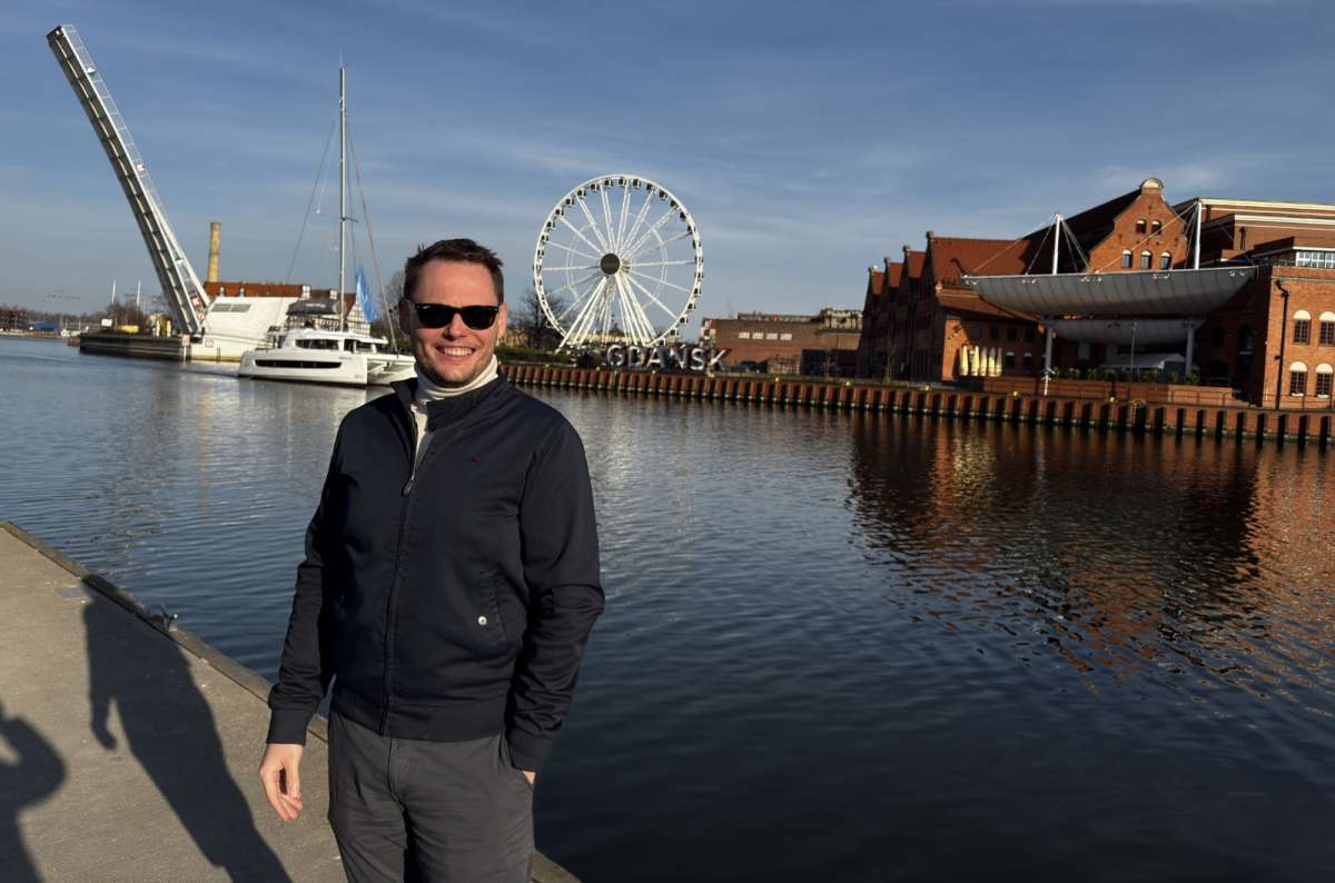 a photo of a tourist posing in front of the Motlawa River at the pier in Gdansk with a Ferris wheel in the background, Gdansk, Poland, photo by Next Level of Travel