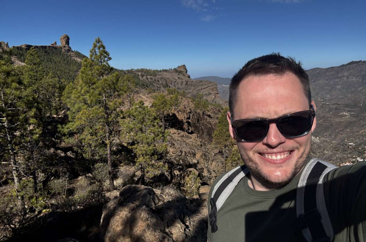 a photo of a tourist posing during a hike, with Roque Nublo visible in the background, Canary Islands, photo by Next Level of Travel