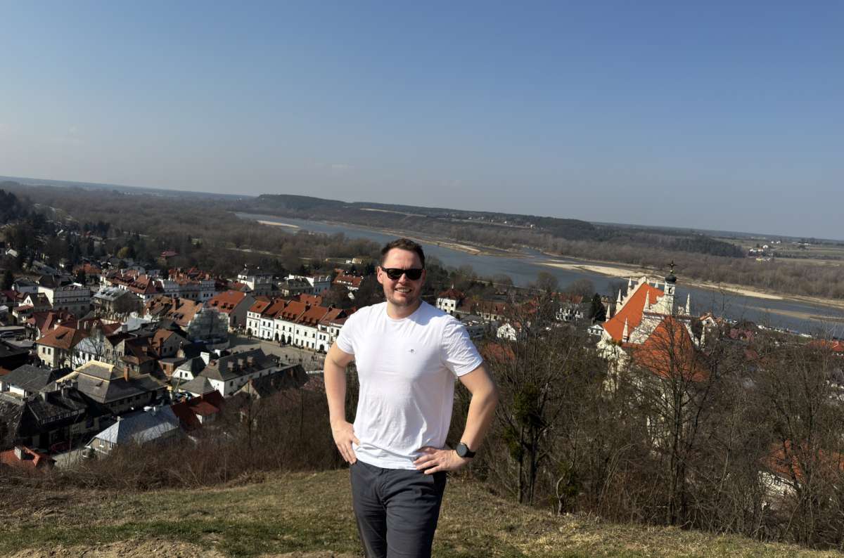 a photo of a tourist on a hill posing in front of the view of Kazimierz Dolny, Poland on a sunny day, photo by Next Level of Travel