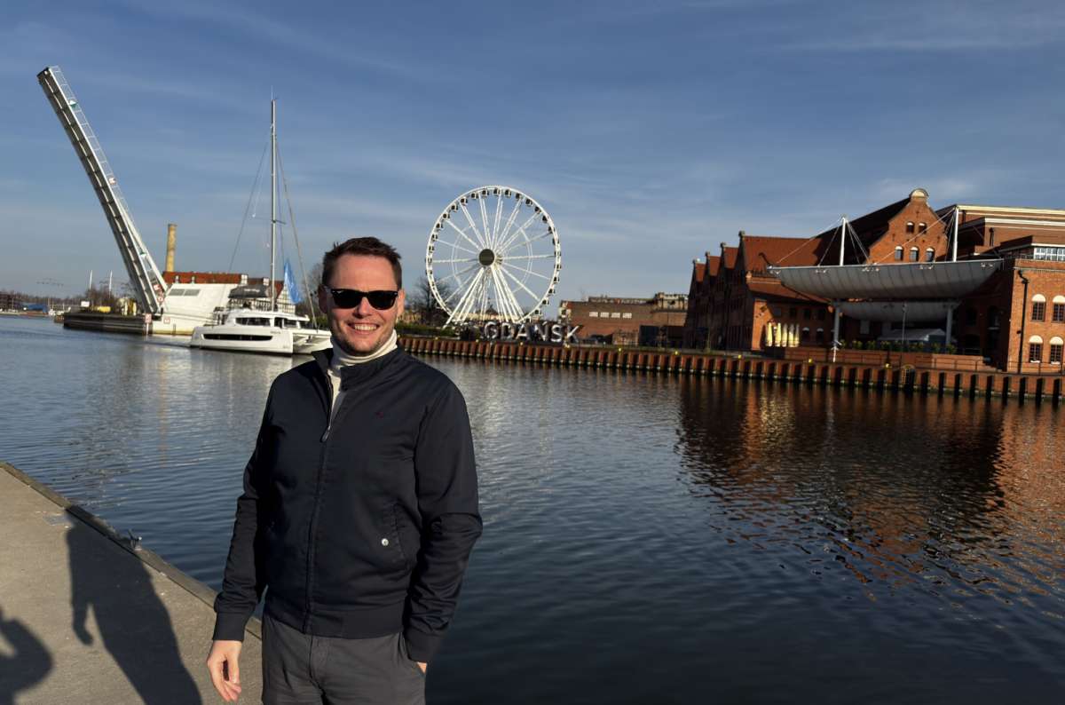 a photo of a tourist posing in front of a Ferris wheel and the river in Gdansk, Poland, photo by Next Level of Travel