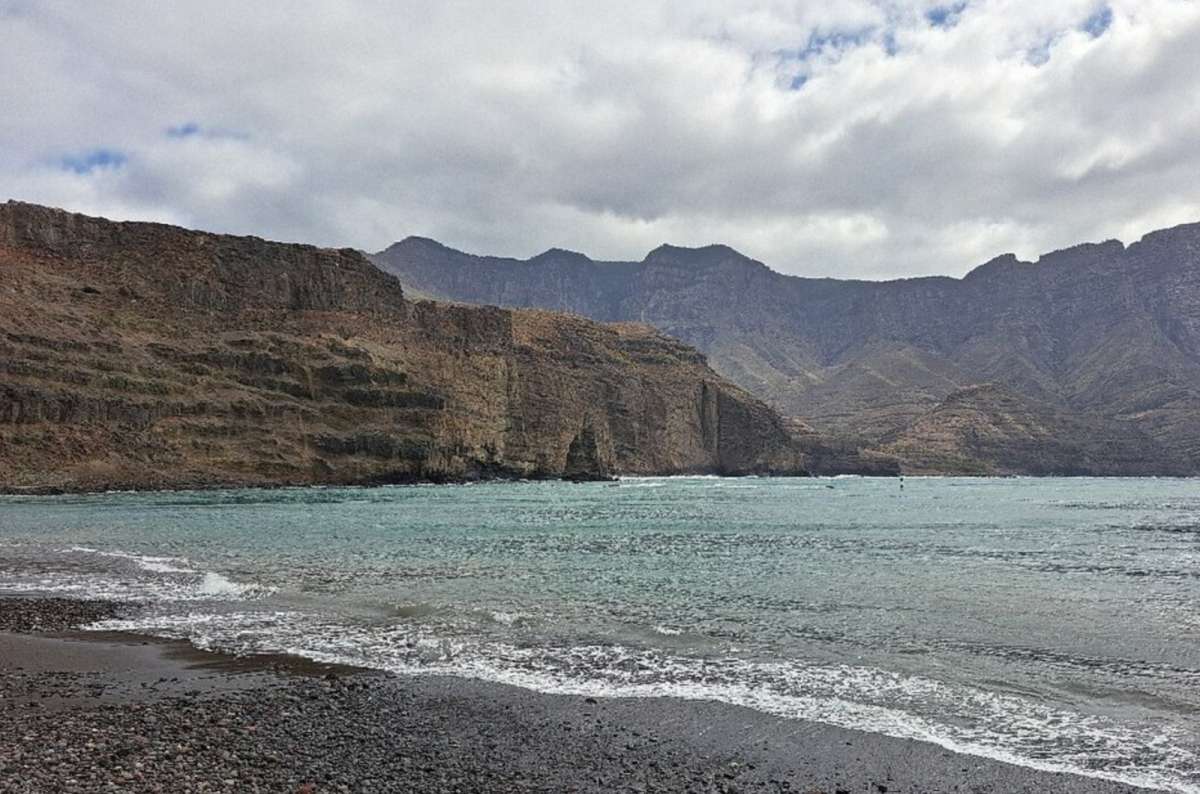  a photo of the Playa de las Nieves Beach, with towering cliffs visible in the background, Canary Island