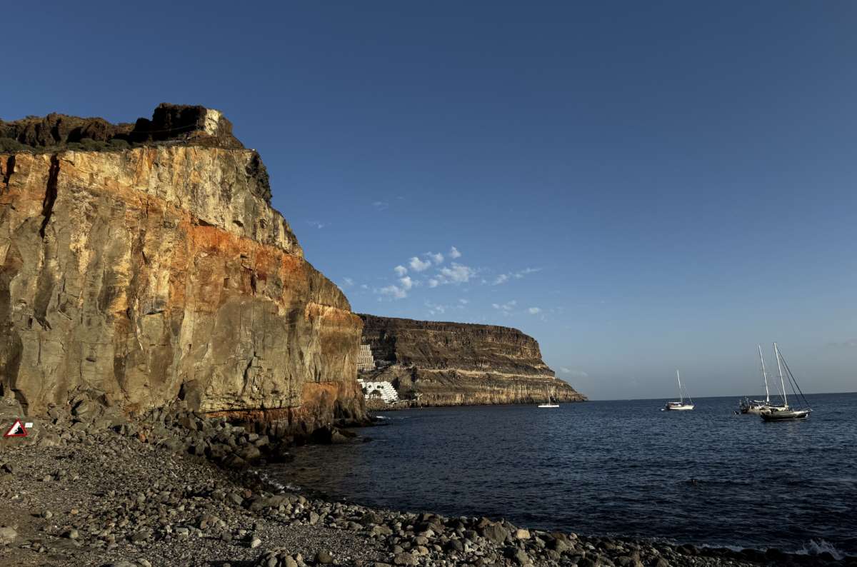 a photo from Playa de Mogán showing the dramatic cliffs and boats in the background, Canary Island, photo by Next Level of Travel