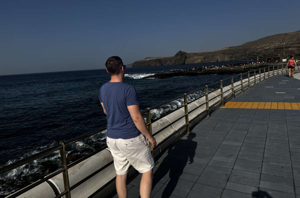 a photo of a tourist standing on the Agaete promenade in Gran Canaria, looking out at the rocky coastline and natural pools, Canary Islands, photo by Next Level of Travel