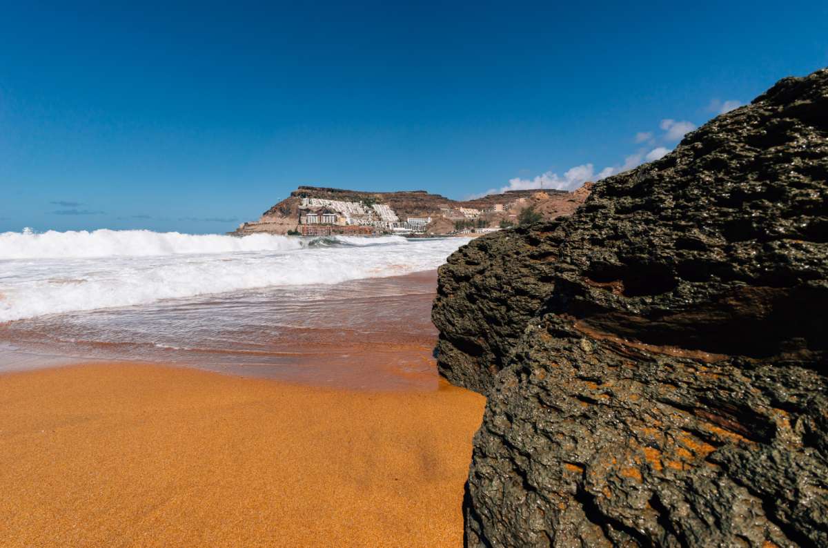 a photo of Playa de Tauro showing the orange sand and the city in the background, Canary Islands