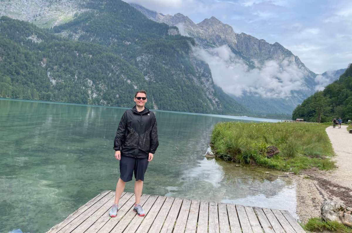 : a photo of a tourist standing by Königssee with mountains and low clouds in Berchtesgaden, Germany, photo by Next Level of Travel