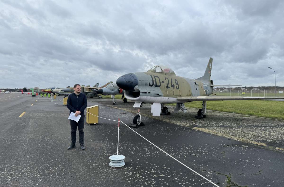 a photo of a tourist posing in front of a plane, exhibited in Berlin, Germany, photo by Next Level of Travel