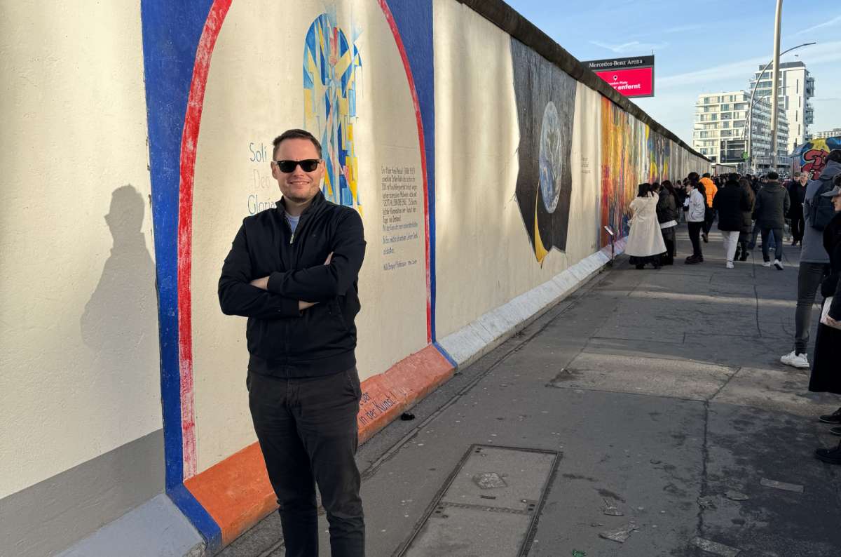a photo of a tourist posing in front of the East Side Gallery with the artwork visible in the background, Germany, photo by Next Level of Travel