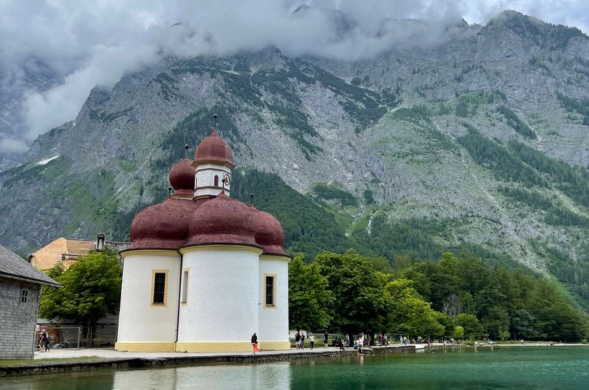 a photo of St. Bartholomä church on the shore of Königssee surrounded by mountains in Bavaria, Germany, photo by Next Level of Travel