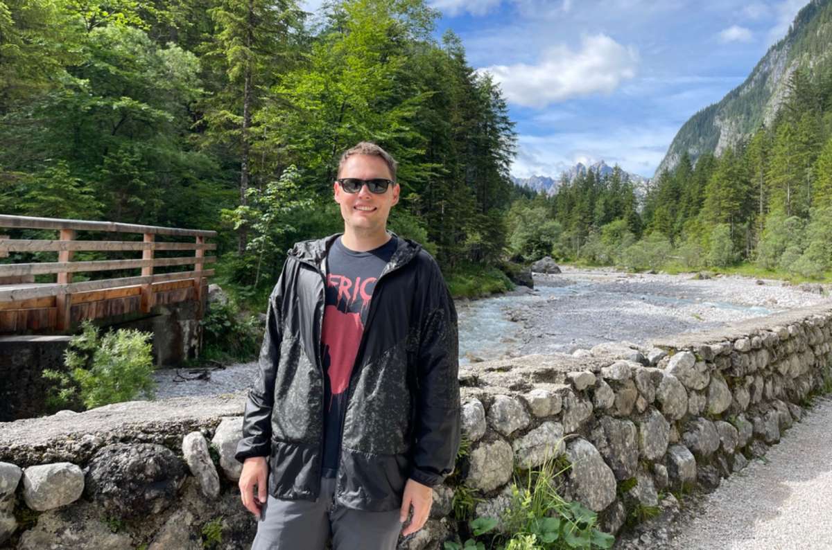 Traveler standing by a mountain river near Königssee in Bavaria, Germany, surrounded by forest and Alpine scenery, photo by Next Level of Travel