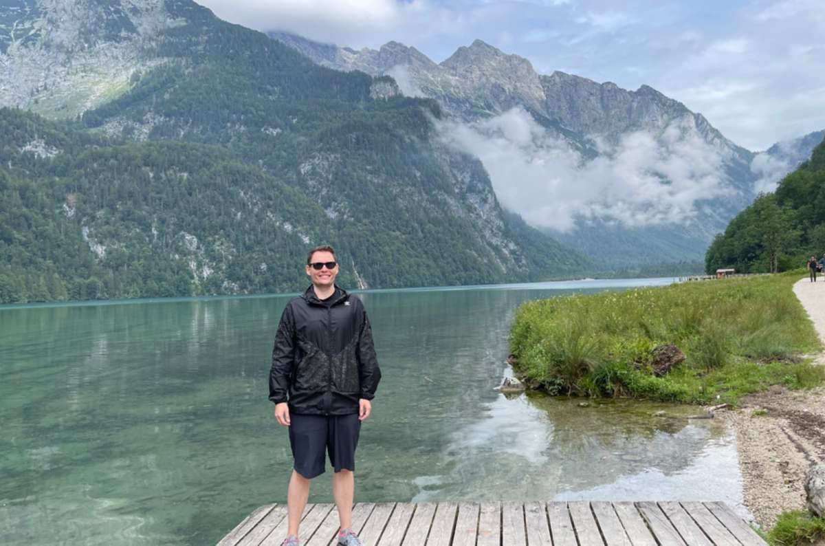 Traveler standing by Lake Königssee in Bavaria, Germany, surrounded by mountains and low clouds, photo by Next Level of Travel