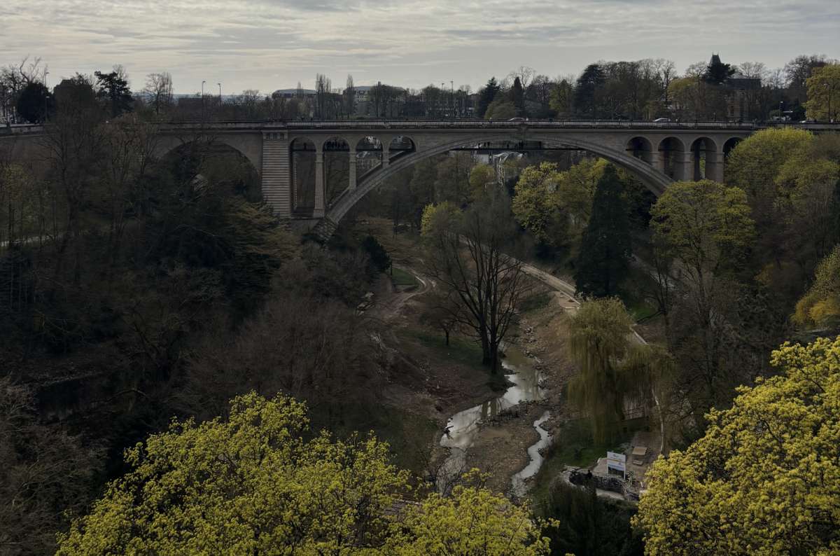 a photo of the Adolphe Bridge spanning the wooded Pétrusse valley, surrounded by green trees, Luxembourg, photo by Next Level of Travel