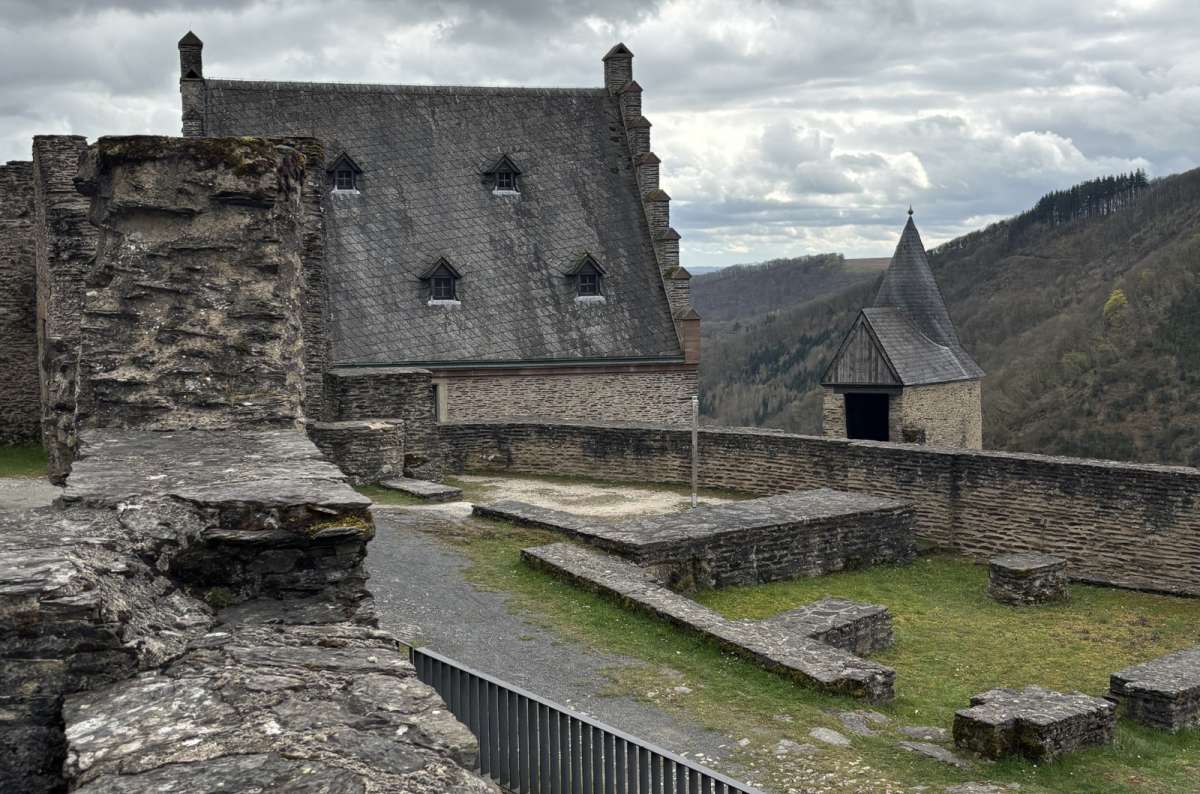 a photo of the Bourscheid Castle courtyard showing the deteriorating ruins with hills and forests visible in the background, photo by Next Level of Travel
